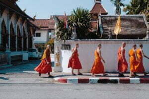 Monks in traditional orange robes walking down a sidewalk in Thailand